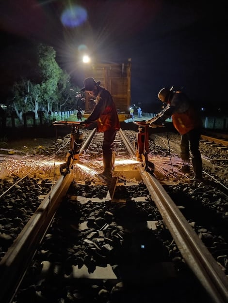A close-up of a construction crew working on a new light rail line in a major US city. The image should highlight the use of modern equipment and safety measures, with city skyscrapers visible in the background.