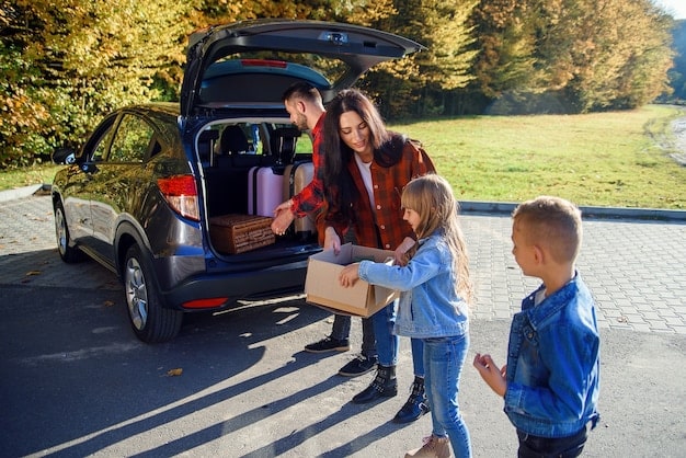 A modern family loading groceries into the trunk of an electric SUV in a suburban setting, with solar panels visible on the roof of their house. The scene highlights the integration of EVs into everyday life and the shift towards sustainable living in suburban communities.